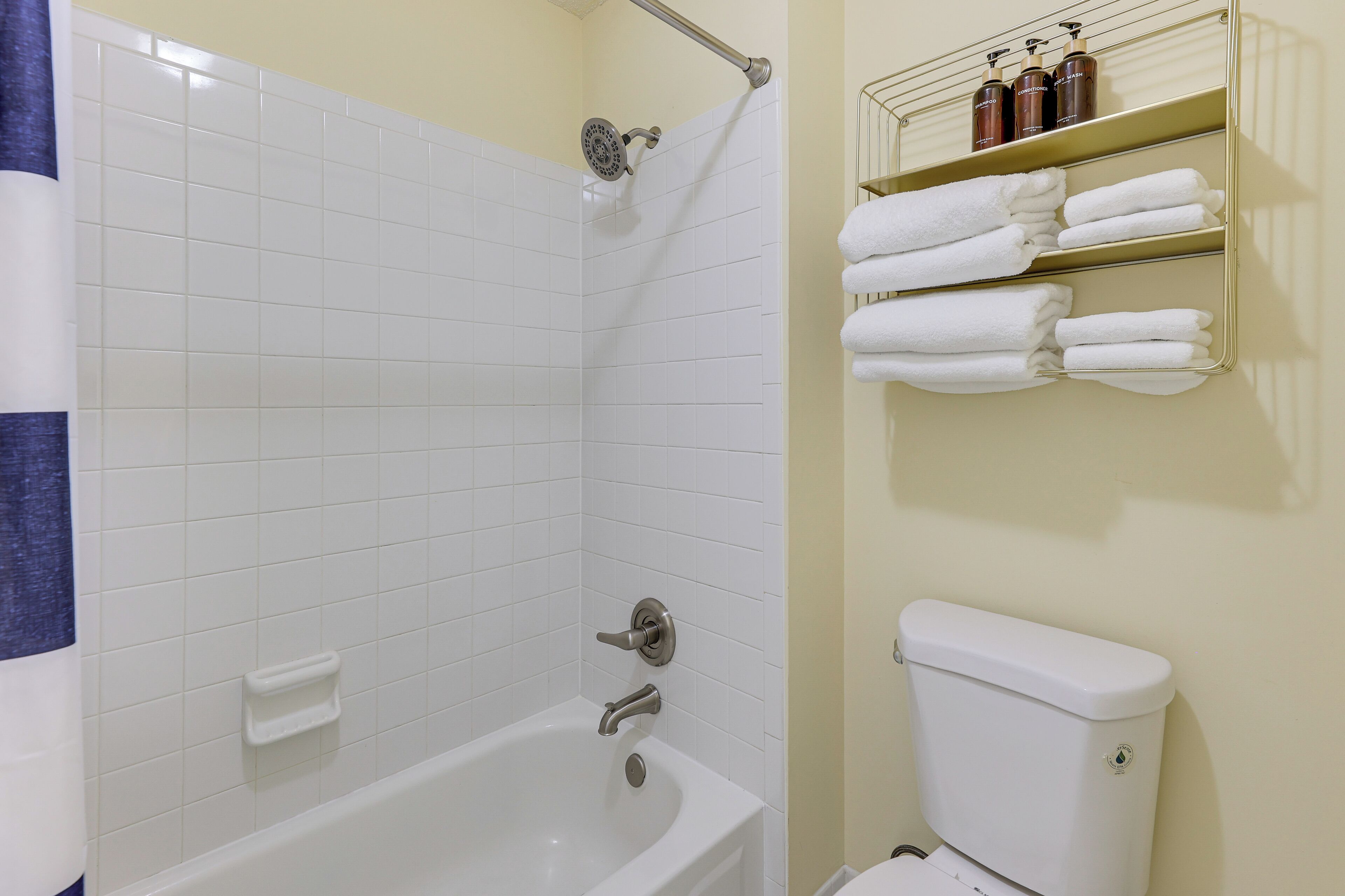 A bathroom with a white bathtub, a shower, and a toilet. There are shelves with towels and toiletries.
