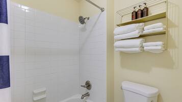 A bathroom with a white bathtub, a shower, and a toilet. There are shelves with towels and toiletries.