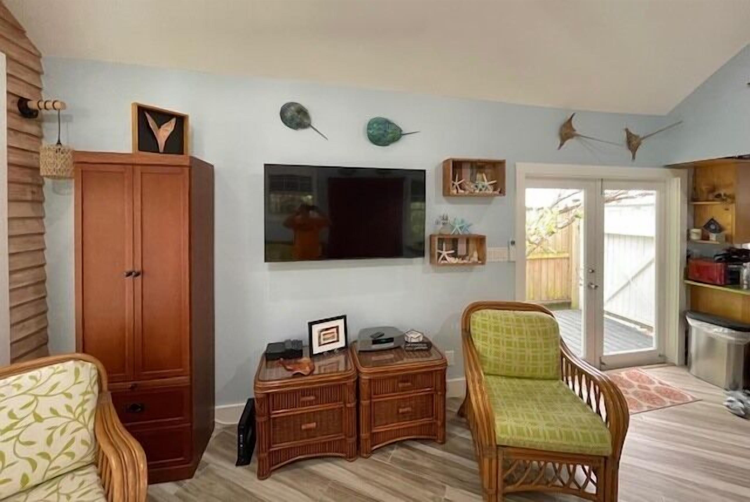 A living room with a wooden cabinet, wicker furniture, a flat-screen TV, and decorative wall art.