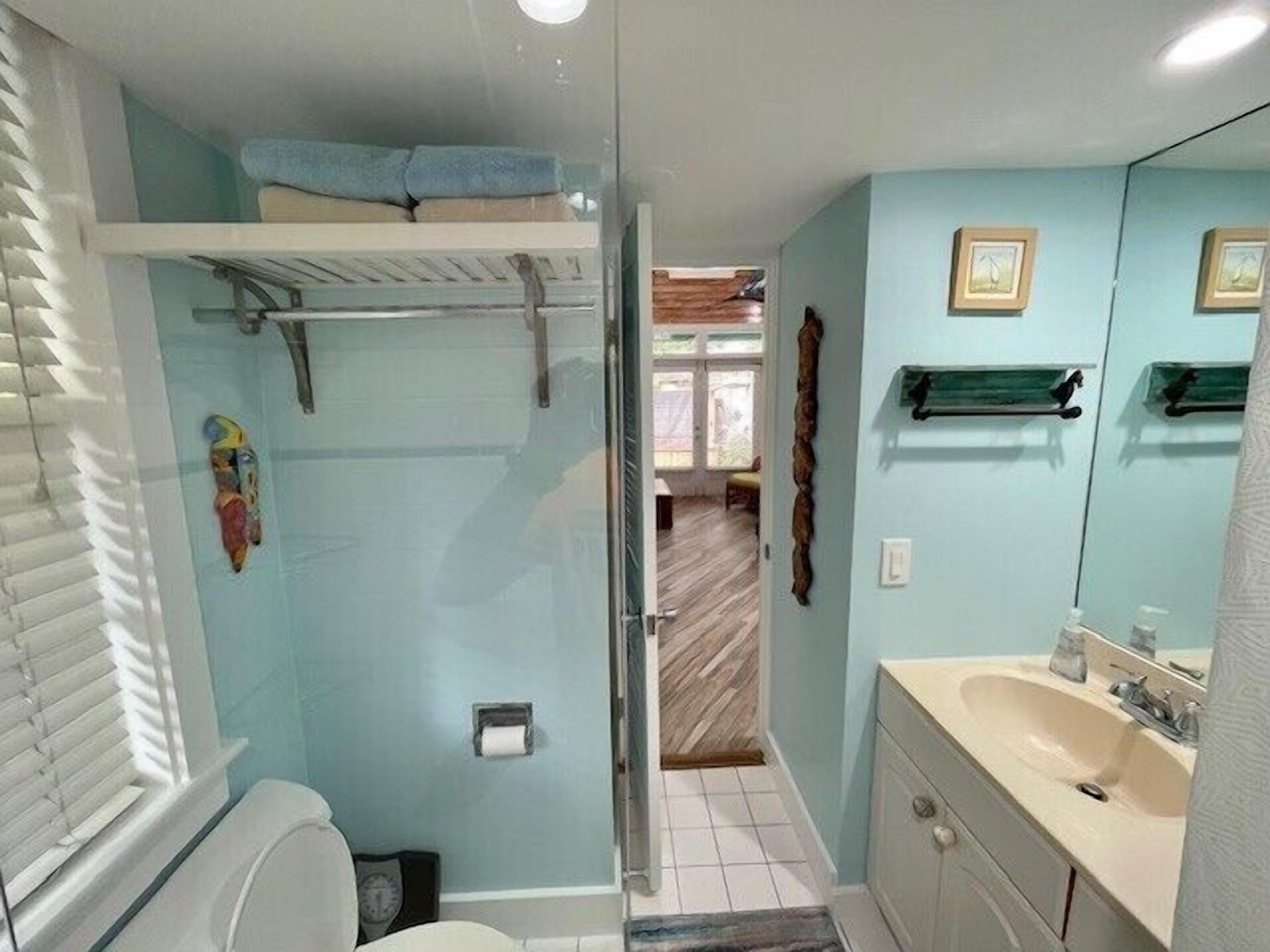 A bathroom with a shower, toilet, sink, and a small window.