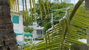 A view of a coastal area with a lighthouse in the background, palm trees in the foreground, and residential buildings with green awnings. - Charming Old Town Studio- Steps to Duval Key West (Key West)