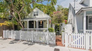 A white house with a porch, surrounded by a white picket fence, and a tree with green leaves. - Charming Old Town Studio- Steps to Duval Key West (Key West)