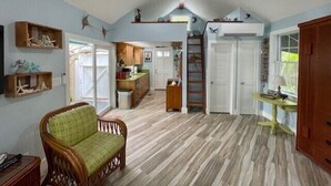 A spacious living area with a high ceiling, wooden flooring, and a green cushioned chair. - Charming Old Town Studio- Steps to Duval Key West (Key West)