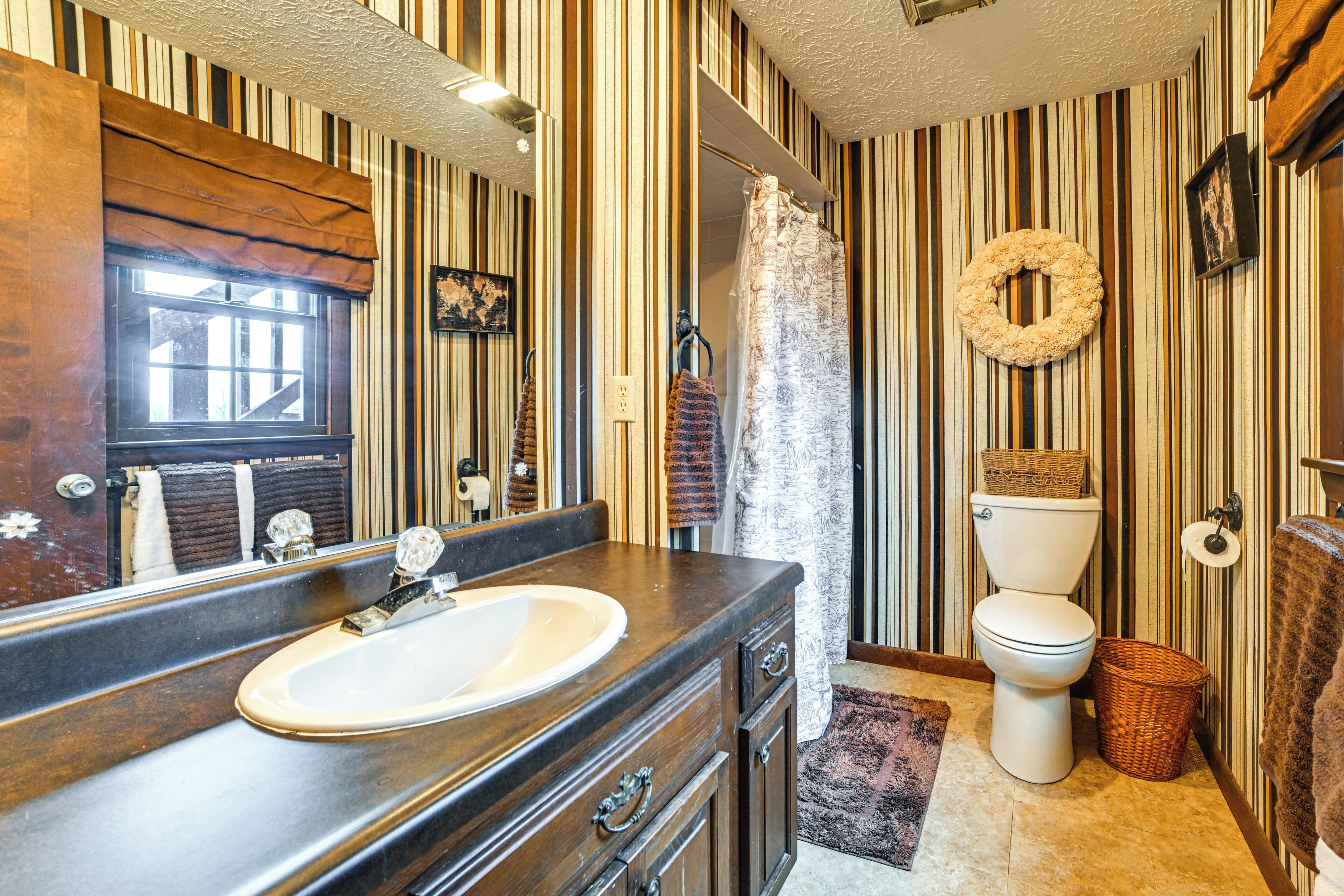 A bathroom with a wooden vanity, a large mirror, a toilet, and striped wallpaper.