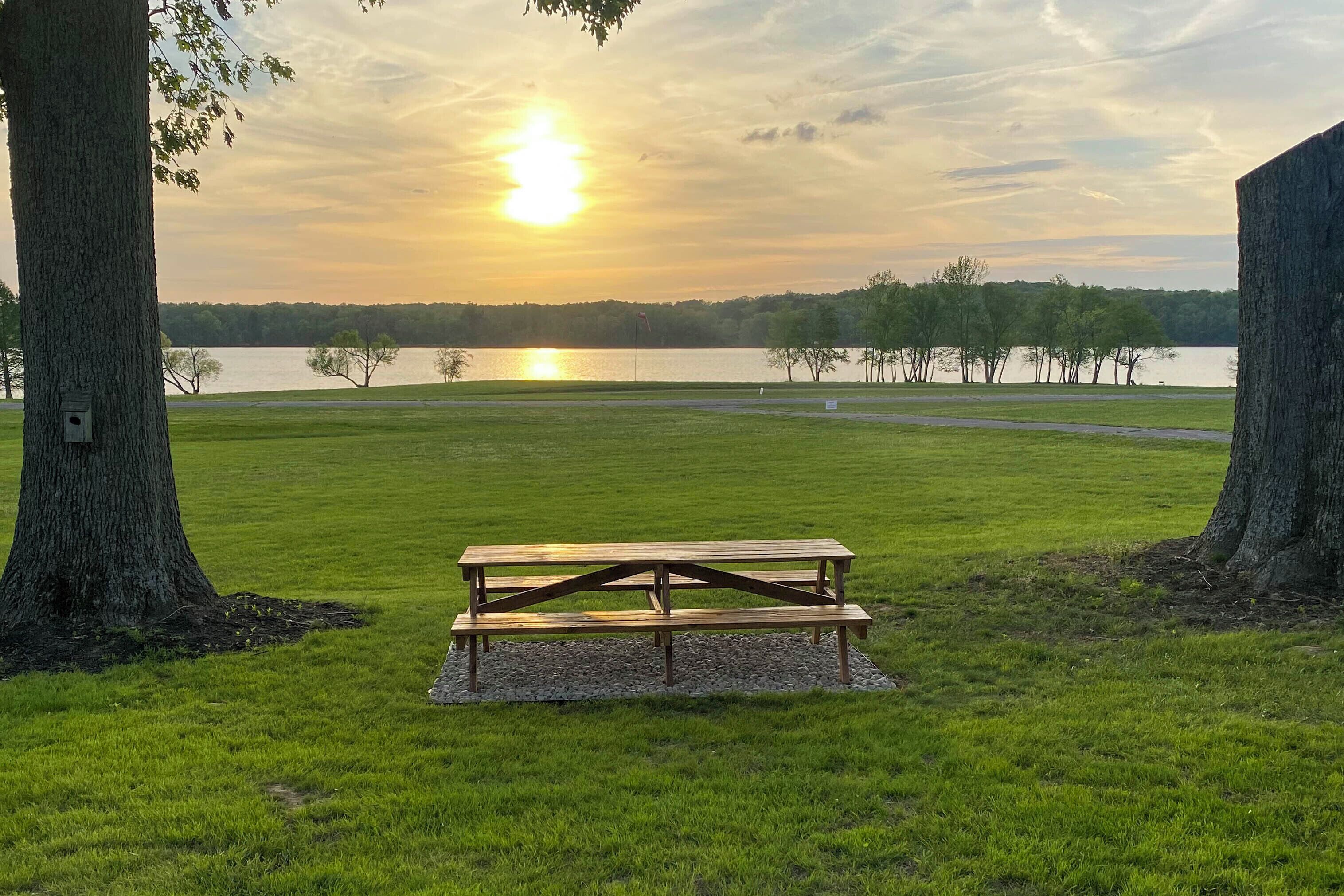 A picnic table in a grassy area with trees and a lake in the background.