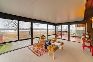 A spacious room with large windows, a wooden rocking chair, a bench, and a small table. - Steps to Shore: Group Getaway on Kentucky Lake! (Hardin)