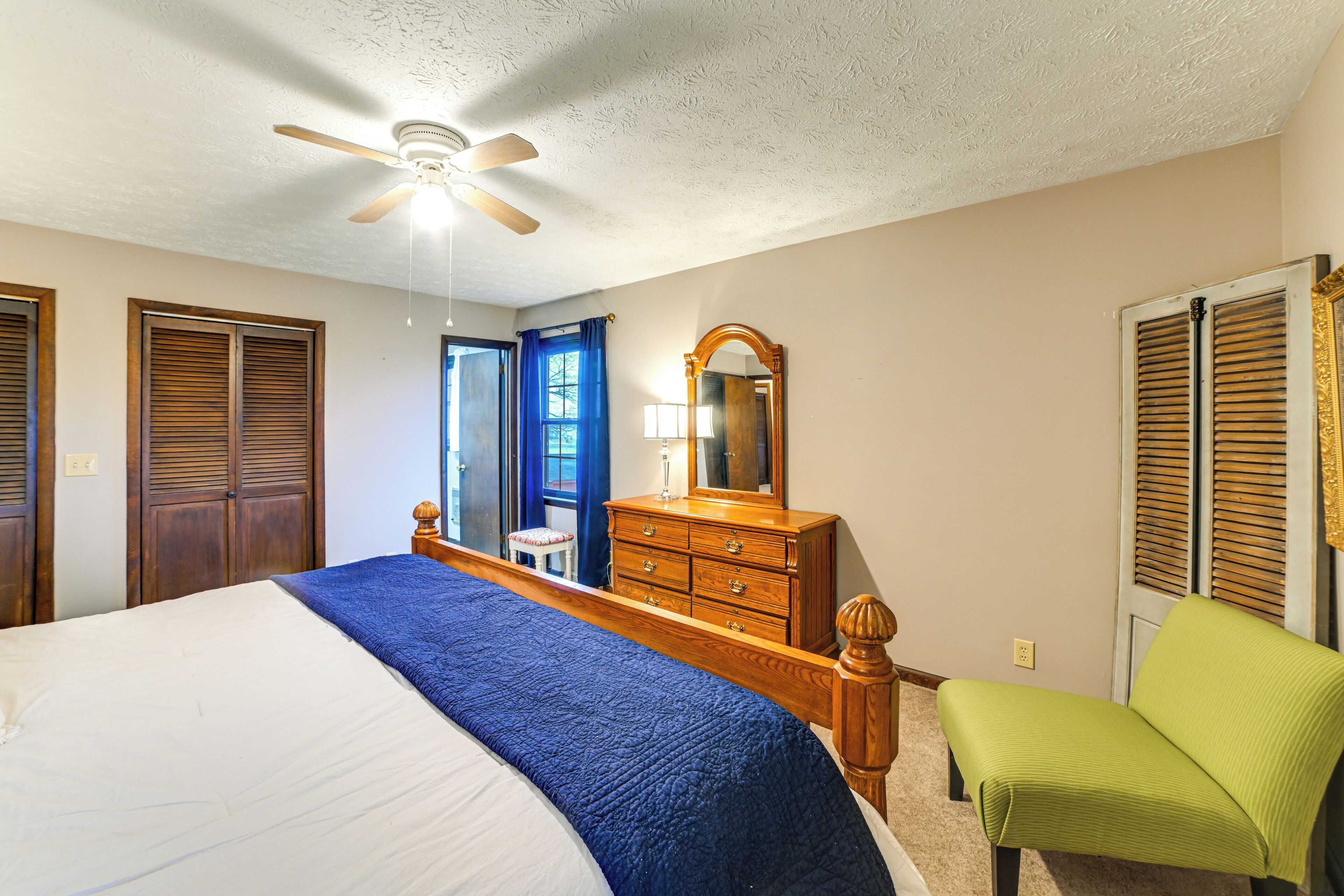 A bedroom with a bed, dresser, chair, and a ceiling fan.