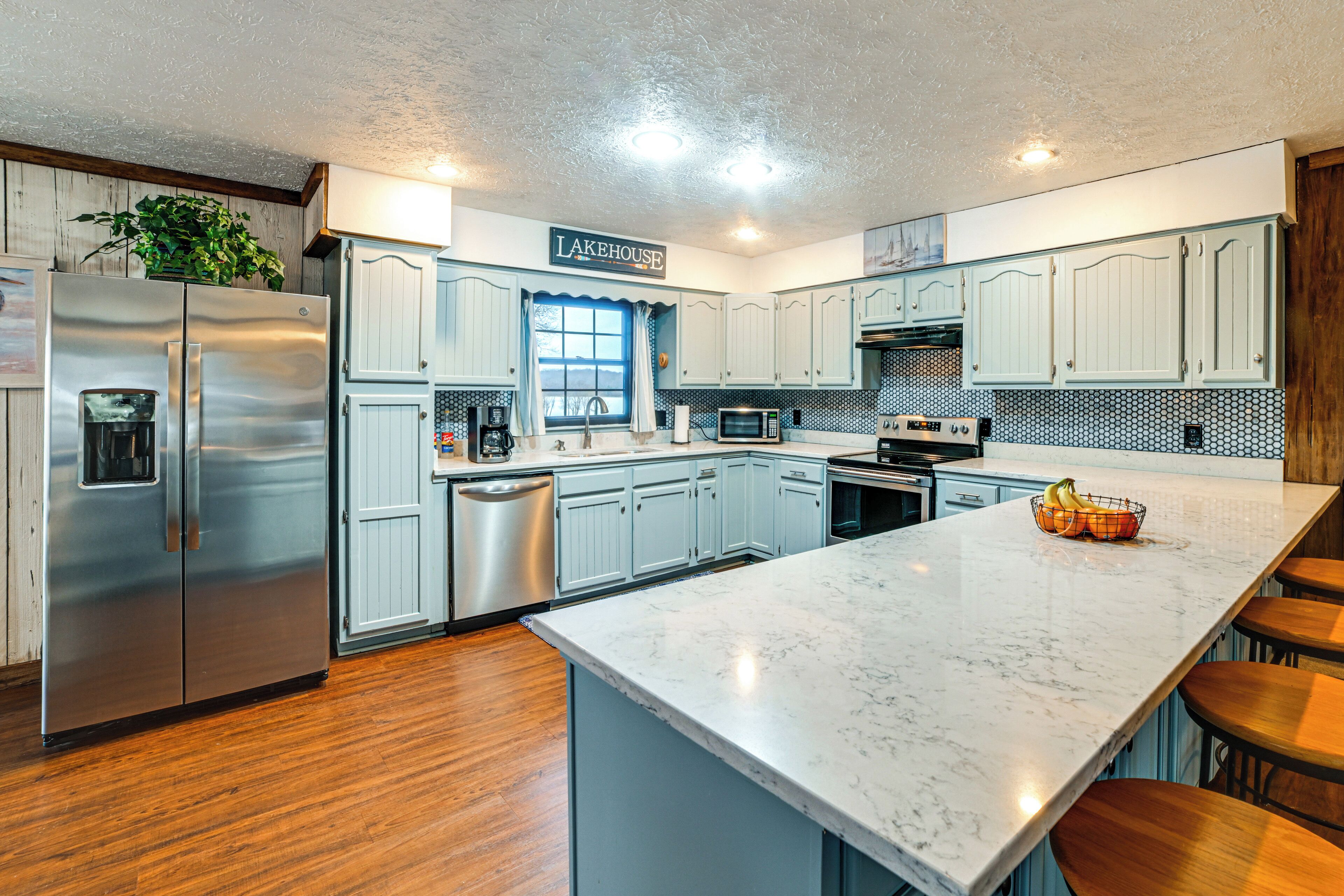 A modern kitchen with stainless steel appliances, light blue cabinets, and a marble countertop.