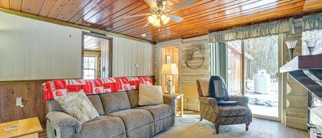 A cozy living room with a wooden ceiling, a sofa, a chair, and a fireplace.