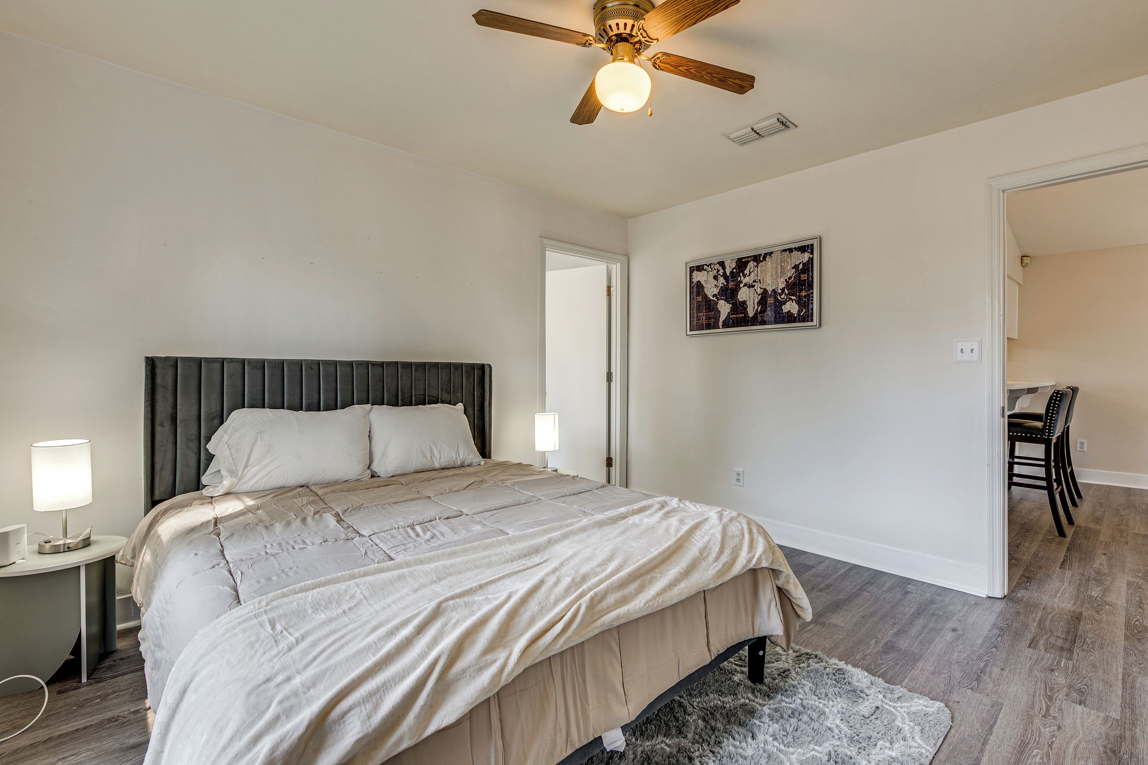 A bedroom with a bed, a nightstand, a ceiling fan, a door, and a chair.