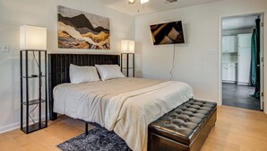 Une chambre à coucher comprenant un lit, des lampes de chevet, un ventilateur de plafond, des œuvres d’art accrochées au mur et une vue sur la pièce adjacente.