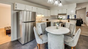 Une cuisine moderne avec des meubles blancs, des appareils en acier inoxydable et une table de salle à manger ronde entourée de chaises grises.