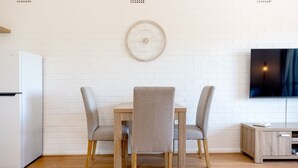 A modern kitchen with a white refrigerator, a dining table with four chairs, and a wall-mounted clock. - Stirling Breeze – One Bedroom Apartment Near Beach & Transport (Mosman Park)