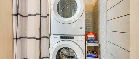 Une petite buanderie équipée de deux machines à laver superposées et d’une étagère contenant des produits de nettoyage.