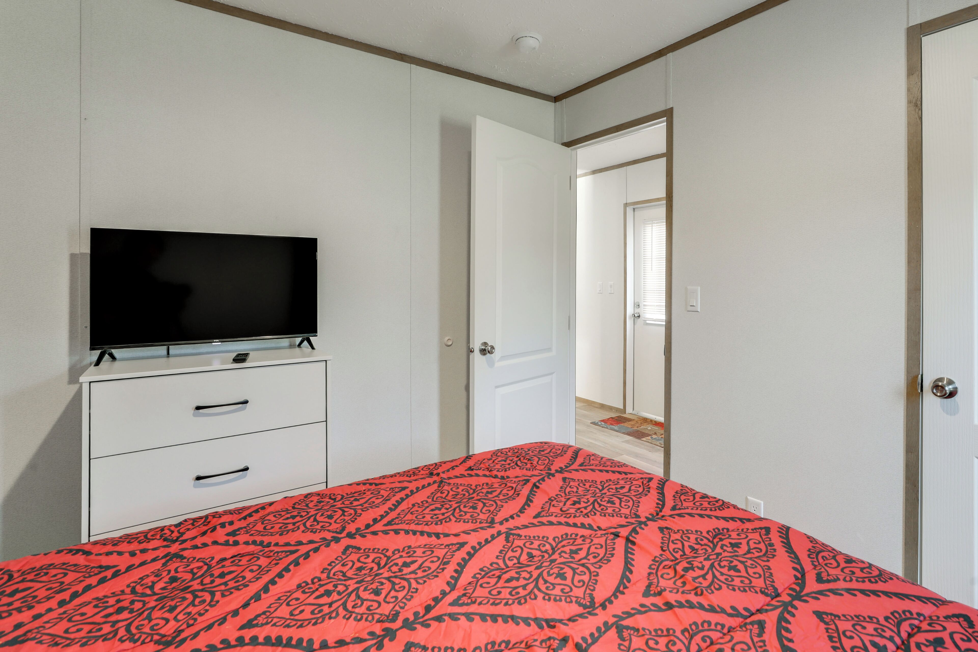 Une chambre à coucher avec un lit, un téléviseur posé sur une commode et une porte donnant sur une autre pièce.