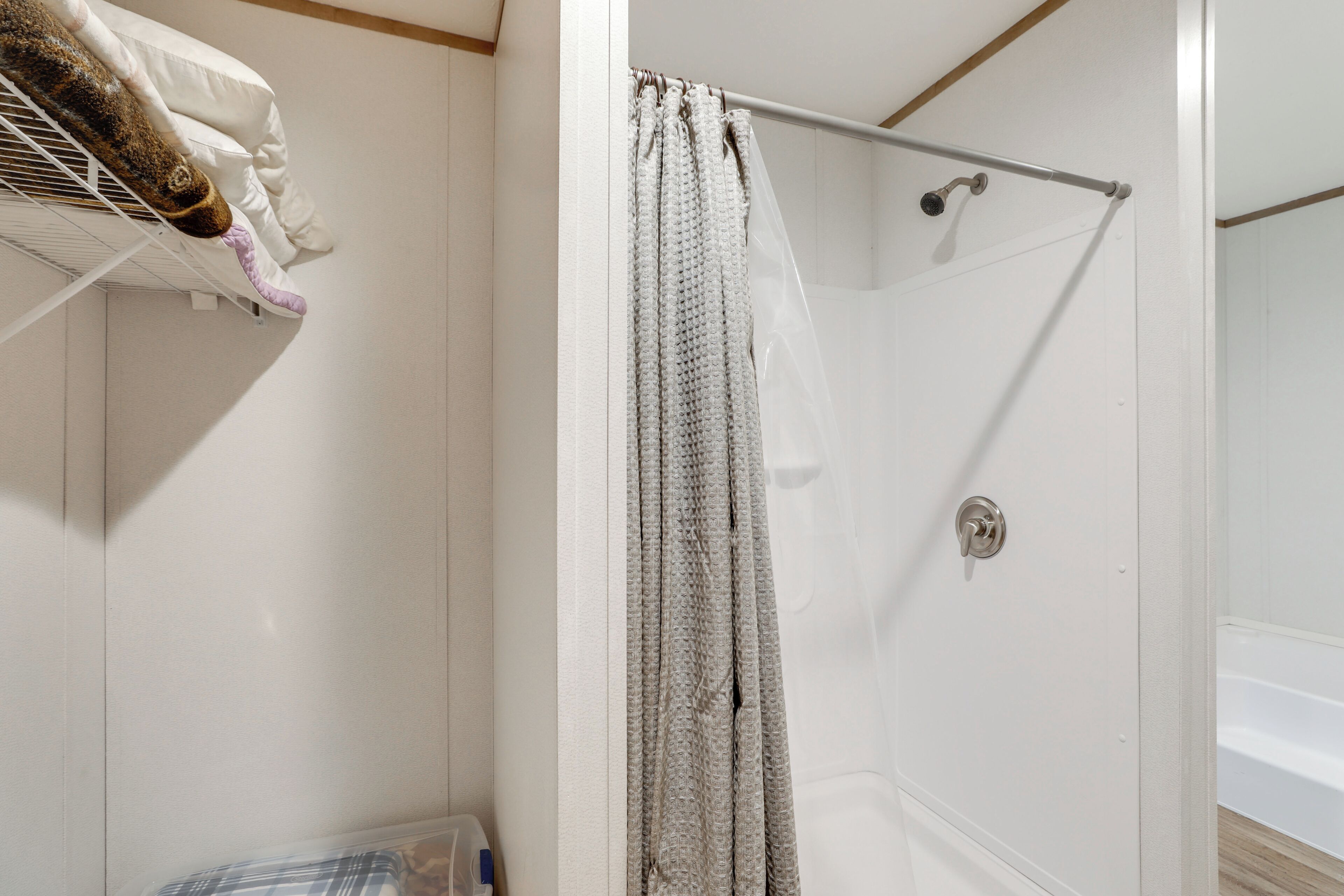 Zona de ducha con puerta blanca, un perchero con toalla y cortina de baño.