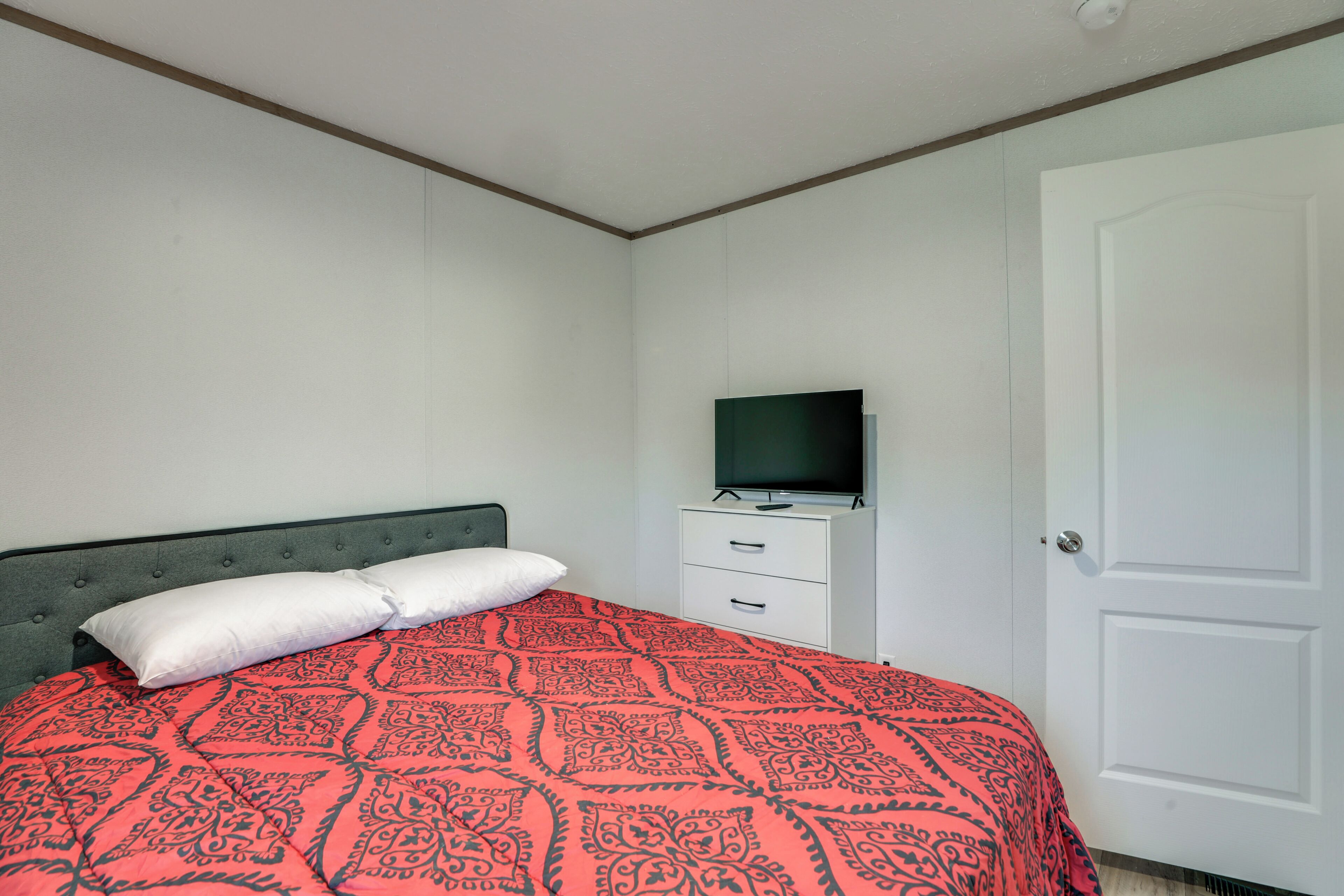A bedroom with a bed, a television on a dresser, and a white door.