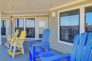 A covered porch with blue and yellow Adirondack chairs, large windows, and a view of the city skyline. - Beach Getaway on Mustang Island: Pet Friendly! (Port Aransas)