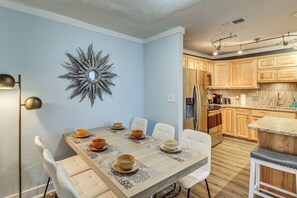 A dining area with a table set for six, surrounded by white chairs. A decorative mirror hangs on the wall above the table. - Beach Getaway on Mustang Island: Pet Friendly! (Port Aransas)
