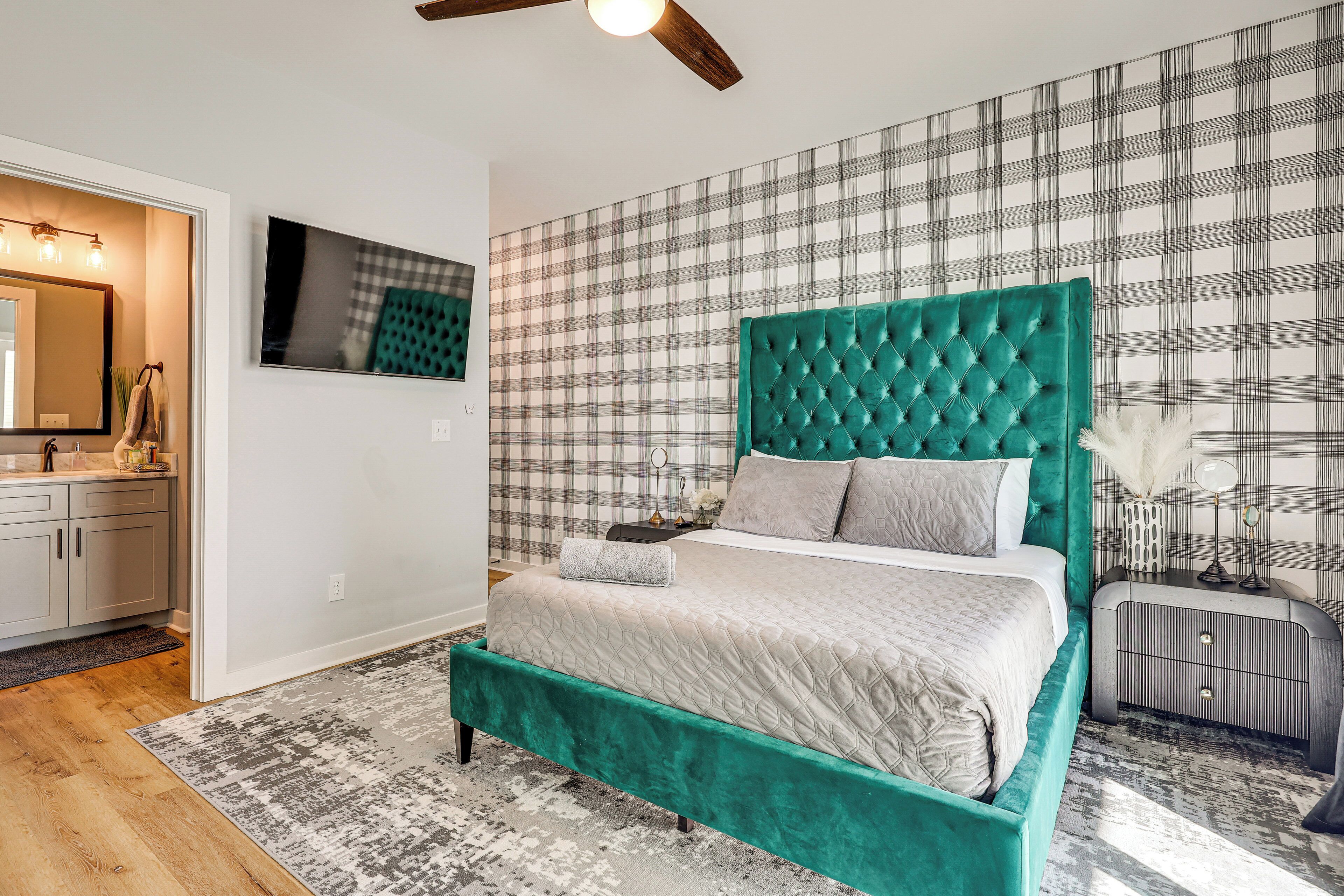 Un dormitorio con una cama grande, una mesita de noche, un aparador, un espejo y una pared con estampado de cuadros.