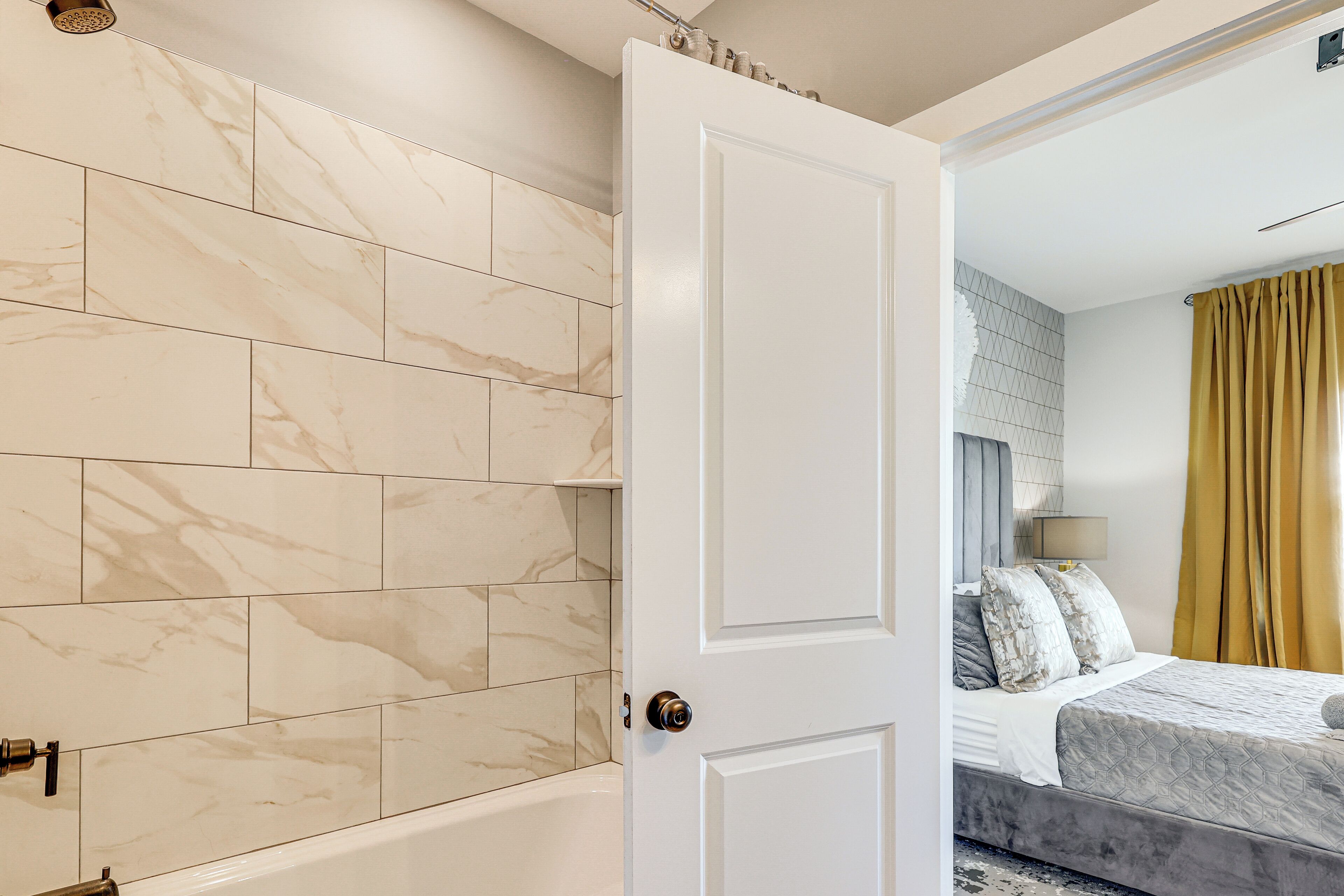 A modern bathroom with marble tiles, a bathtub, and a white door.