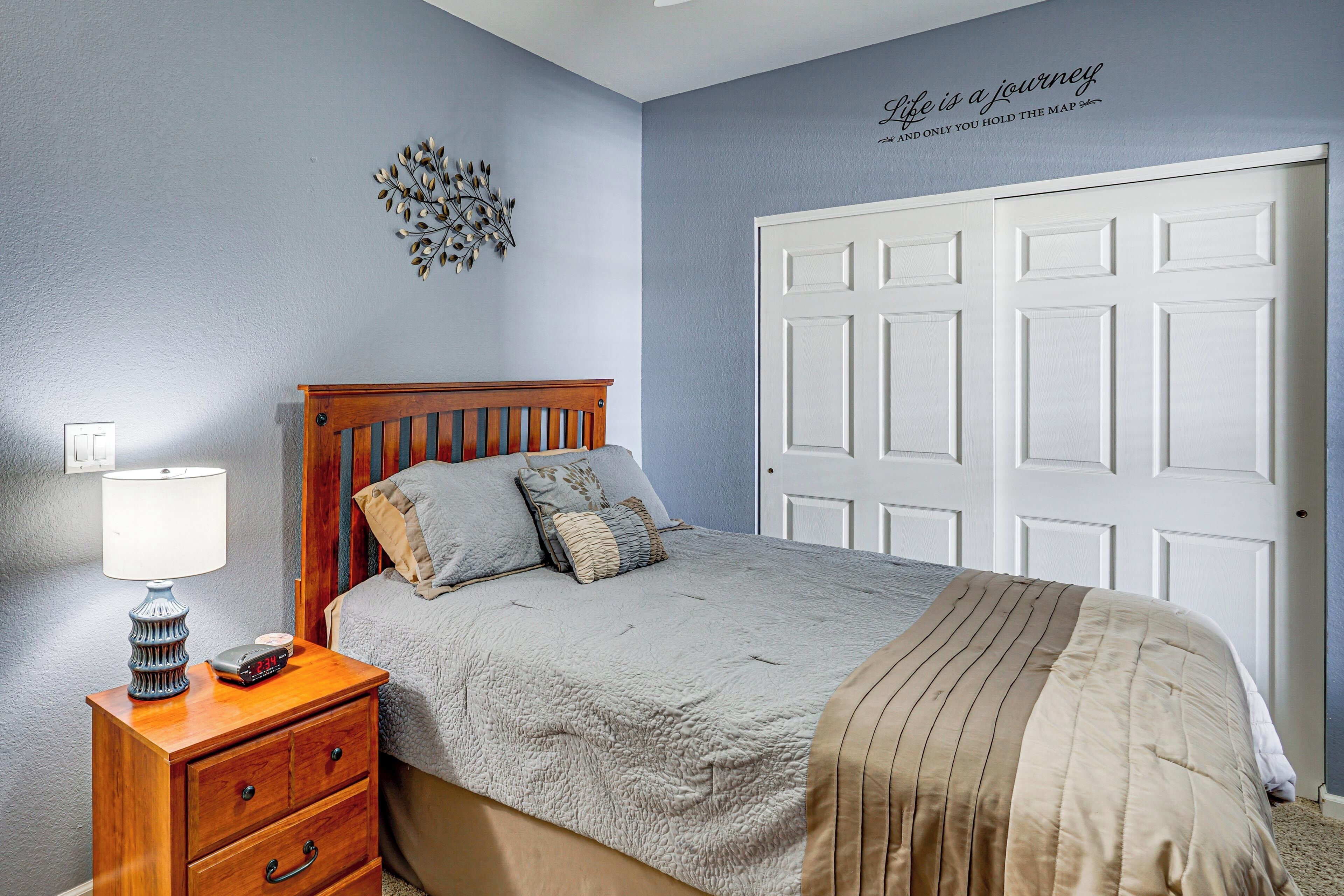 A bedroom with a bed, nightstand, dresser, and a white door.