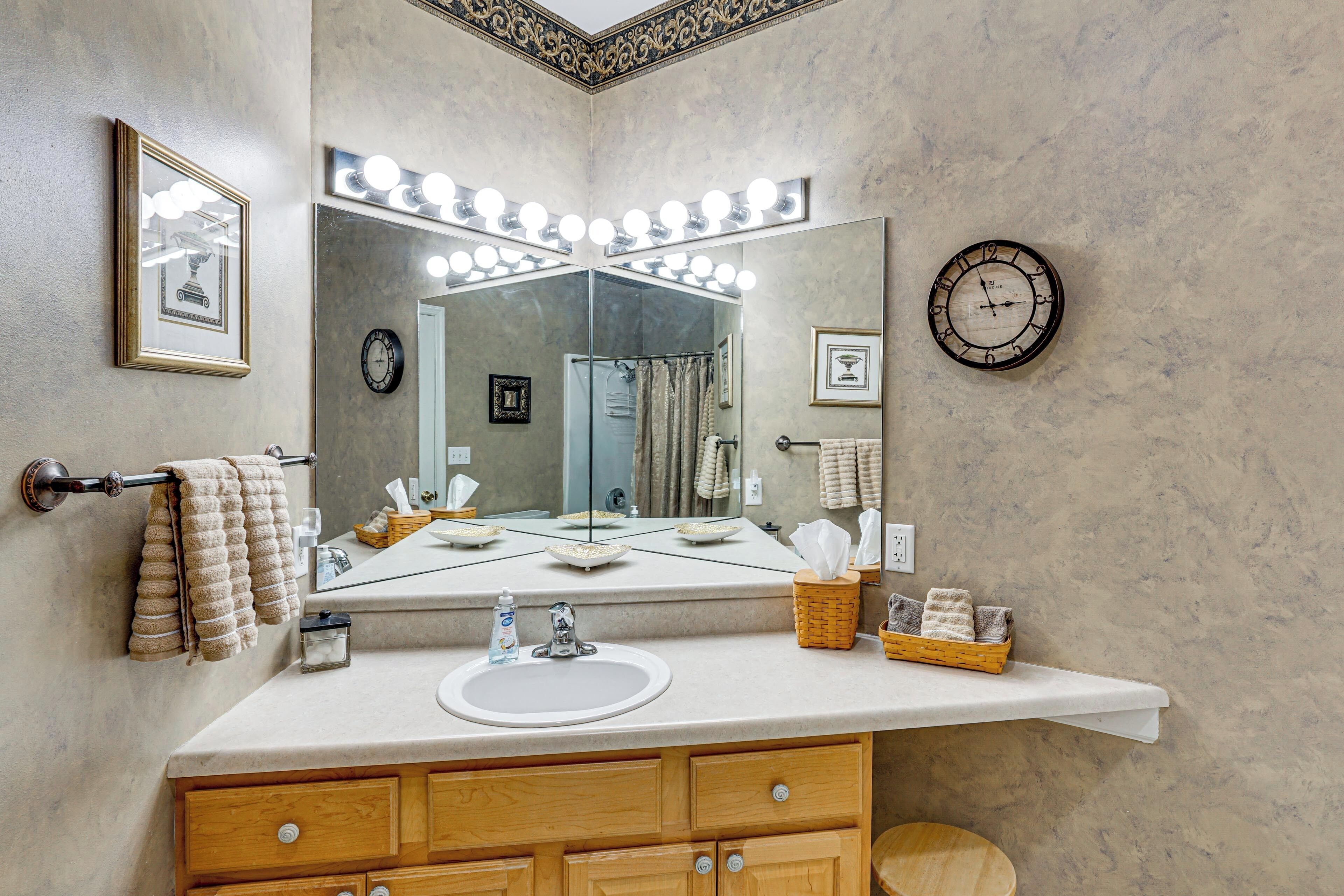 Une salle de bain comprenant un meuble-lavabo, un évier, un miroir avec éclairage, un porte-serviettes, une horloge et des objets décoratifs.