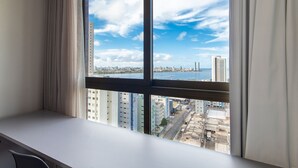 Quarto com uma grande janela que oferece vista para o horizonte urbano, incluindo edifícios e uma ponte.