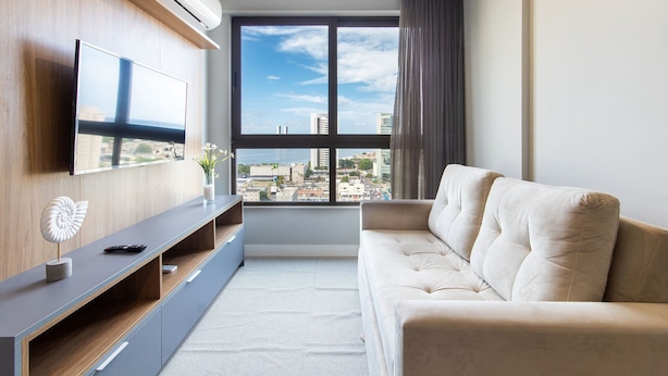 Uma sala de estar moderna com uma janela grande, uma televisão de tela plana, um sofá e uma mesa de apoio com objetos decorativos.