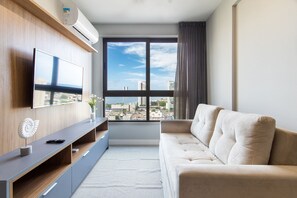 A modern living room with a large window, a flat-screen TV, a sofa, and a console table with decorative items. - Parque Shopping - Apartament Confort by Carpediem (Recife)
