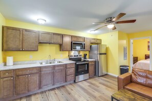 Une cuisine de taille réduite, dotée de meubles en bois, d’appareils électroménagers en acier inoxydable et d’un ventilateur de plafond.