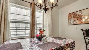 A dining area with a table set for two, a chandelier, and a window with curtains. - 2 Mi to UBS Arena & Belmont Park: Suburban Escape (Elmont)
