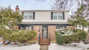 A two-story house with a brick facade, a front door, and a small front yard with snow. - 2 Mi to UBS Arena & Belmont Park: Suburban Escape (Elmont)