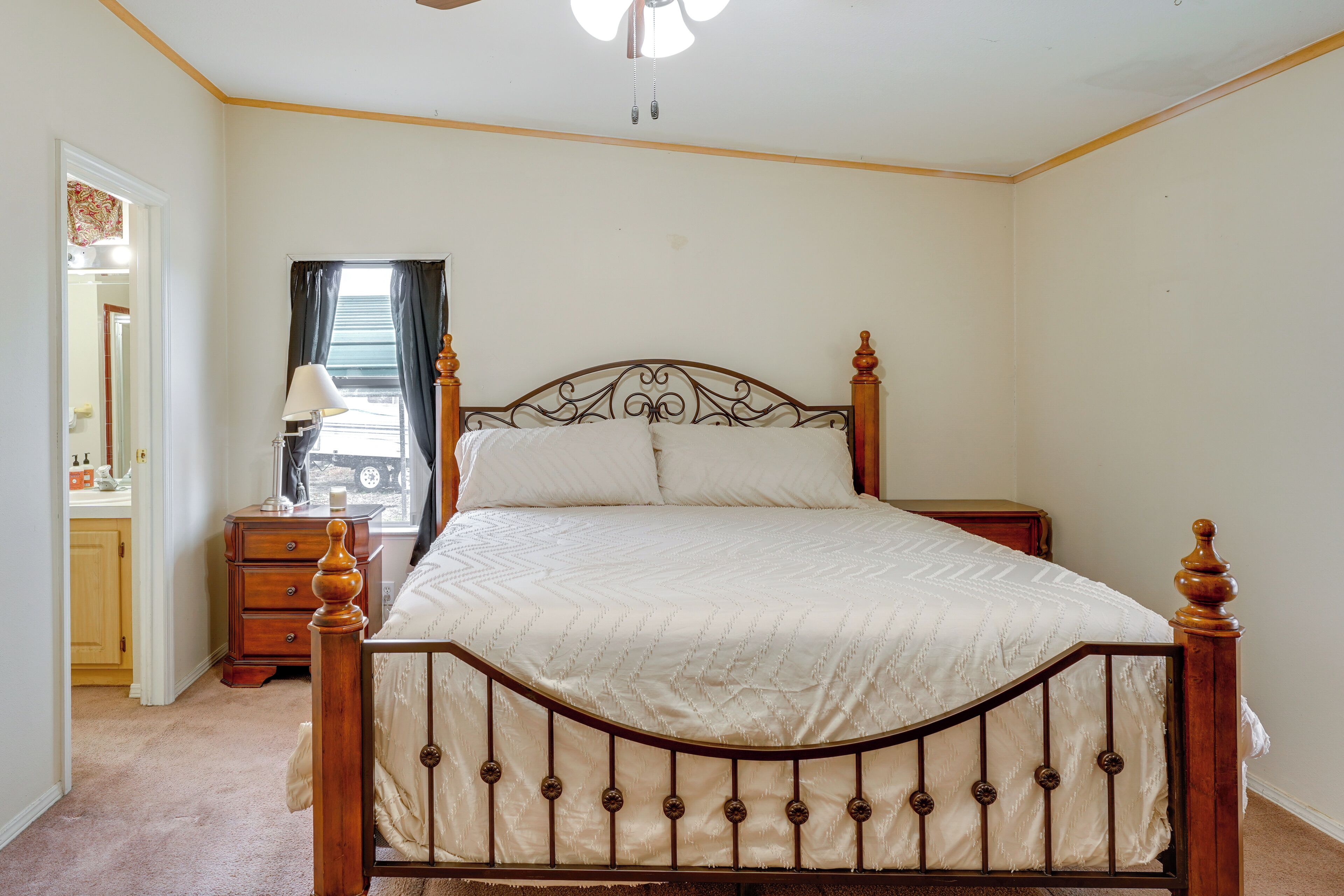 A bedroom with a wooden bed frame, a nightstand, a dresser, and a window with curtains.