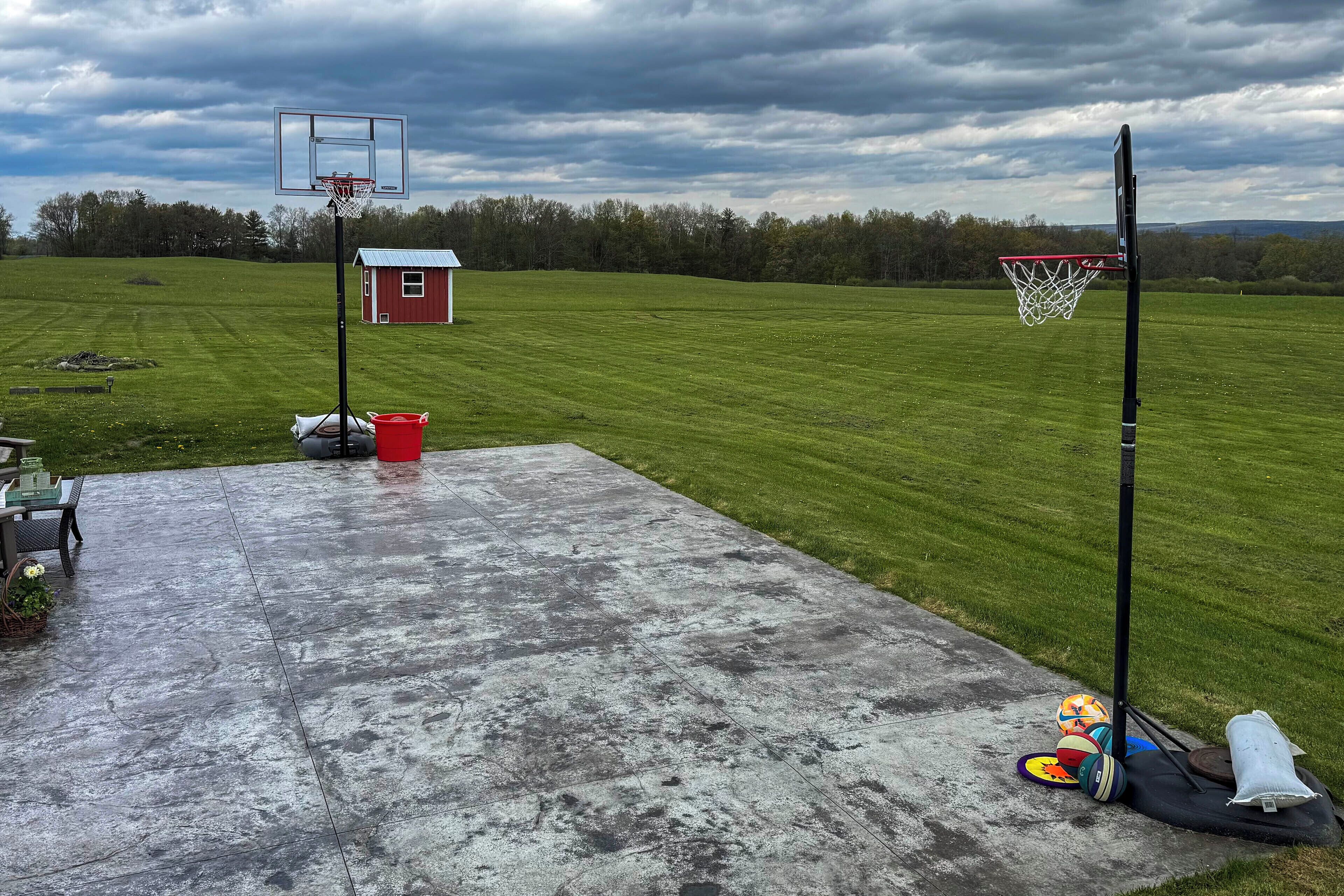 Ein Basketballplatz mit Korb, eine rote Holzhütte und ein Rasenfeld.