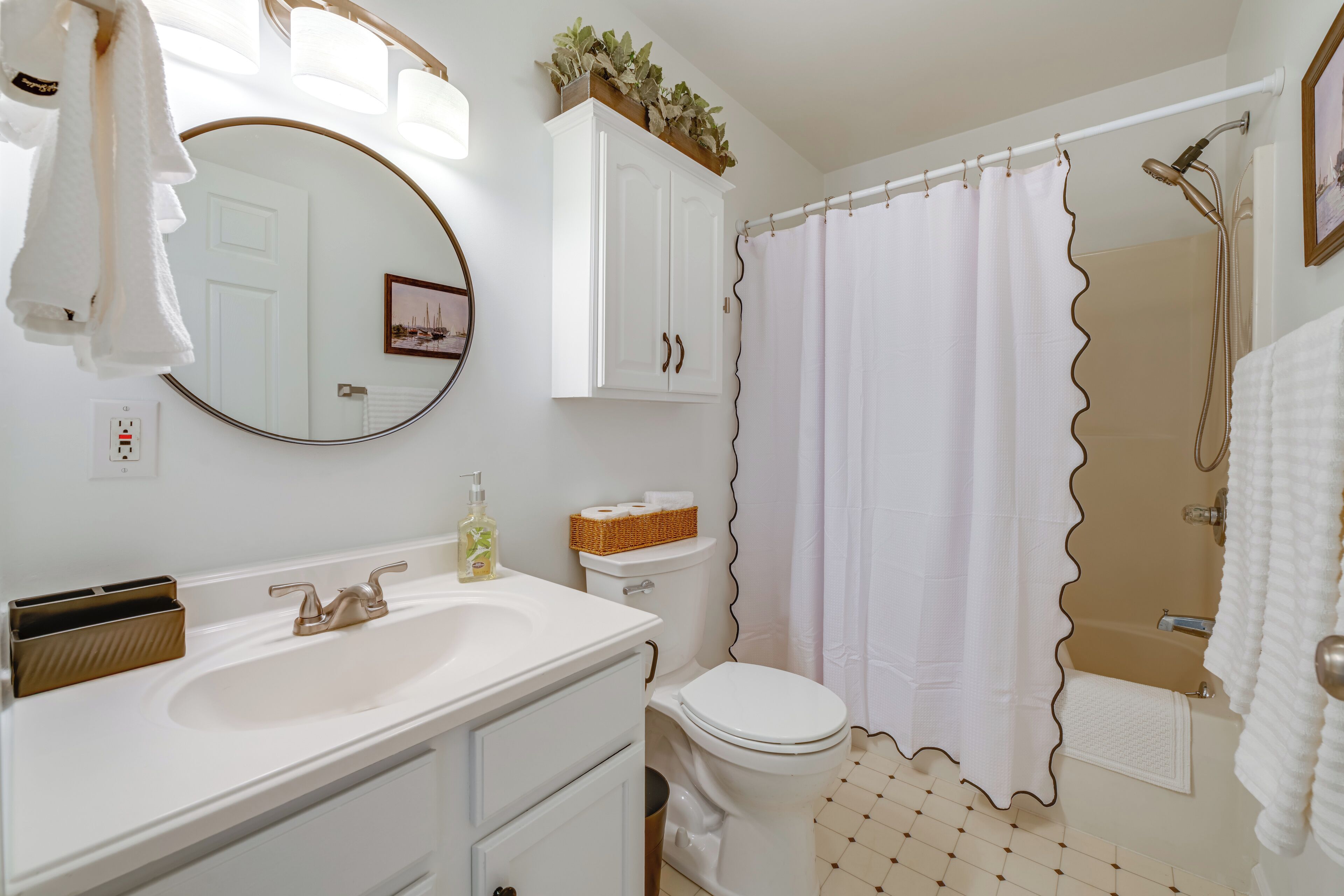 A bathroom with a white sink, toilet, and shower curtain. There is a mirror above the sink and a cabinet above the toilet.