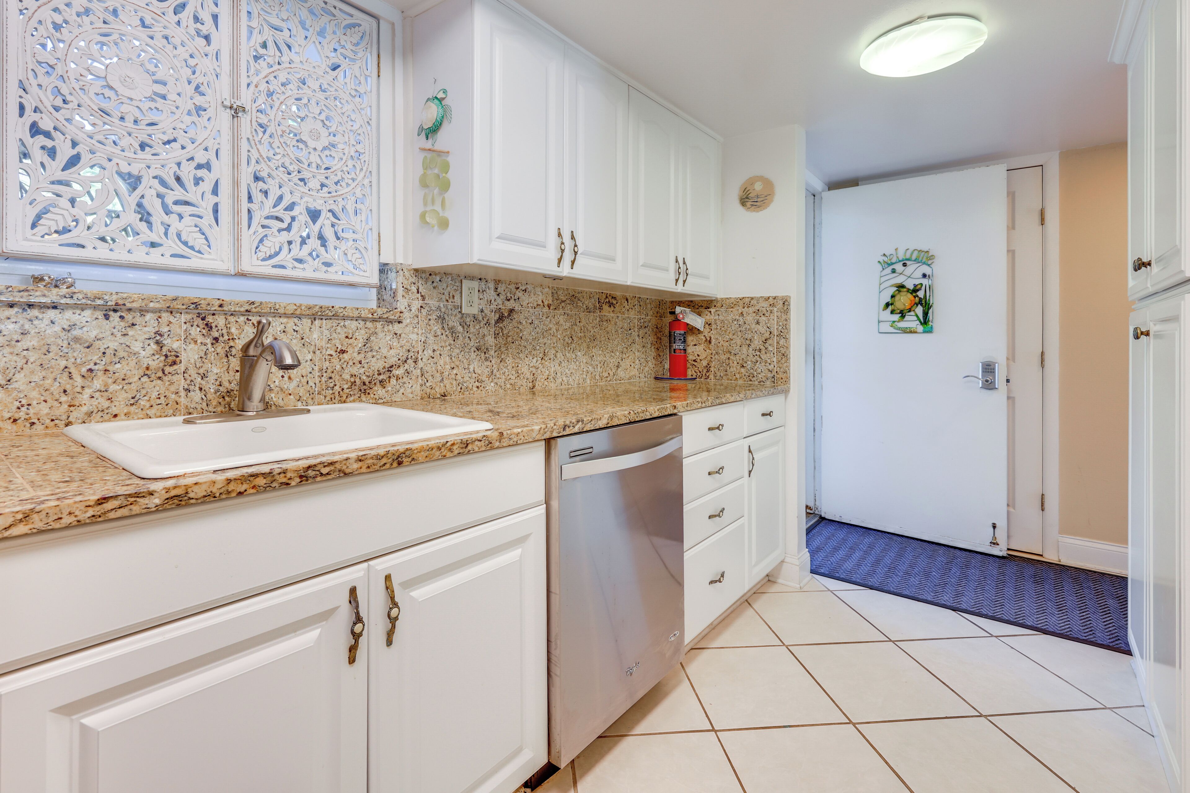 A kitchen with white cabinets, a granite countertop, a stainless steel dishwasher, and a decorative wall panel.