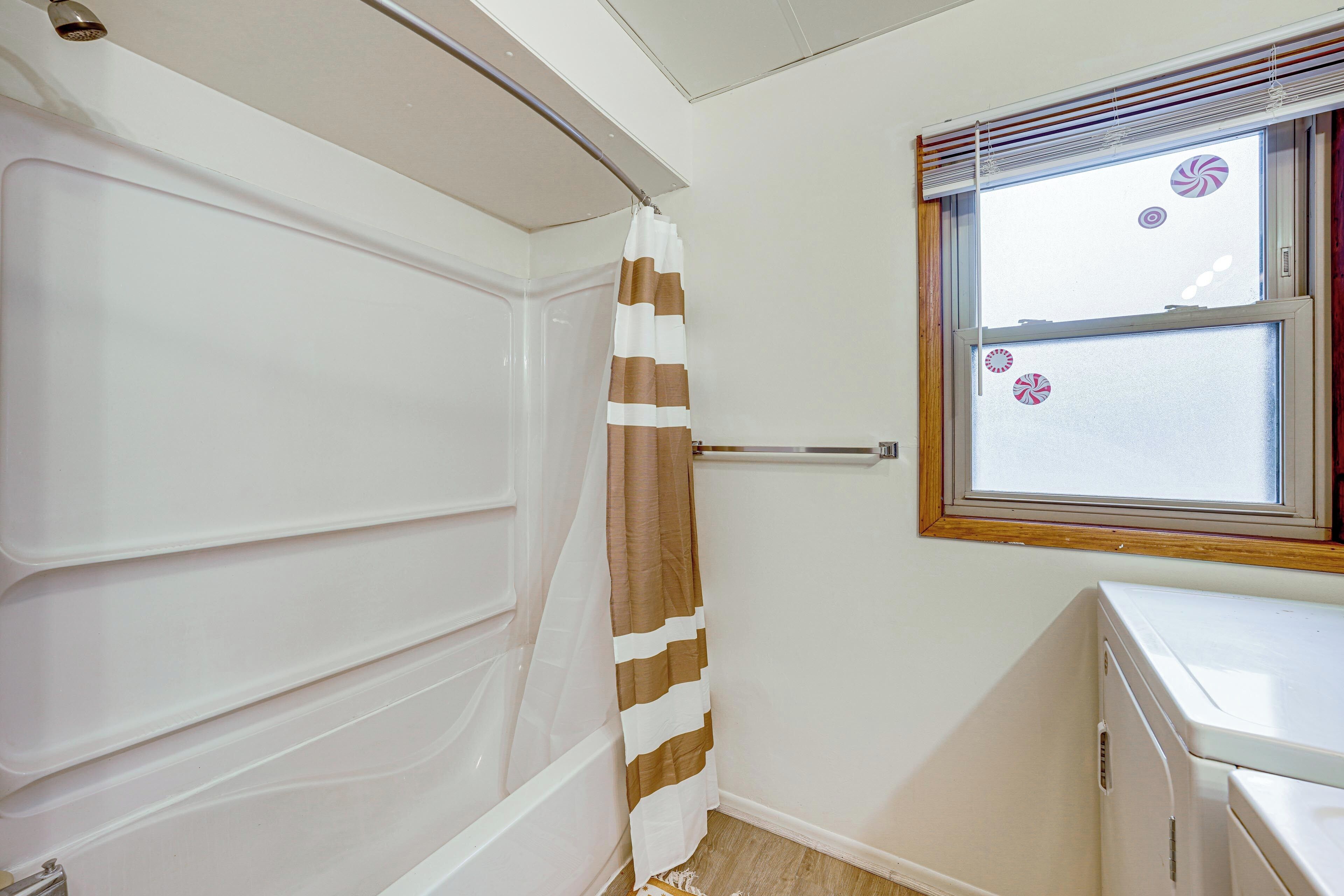 A bathroom with a bathtub, a shower curtain, a window with blinds, and a washing machine.