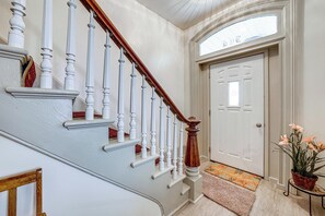 Un escalier avec des balustrades blanches et une main courante en bois menant à une porte blanche surmontée d’une fenêtre.