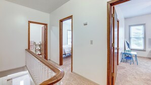 Un pasillo con una escalera de madera, un dormitorio con cama y ventana, y un escritorio con silla.
