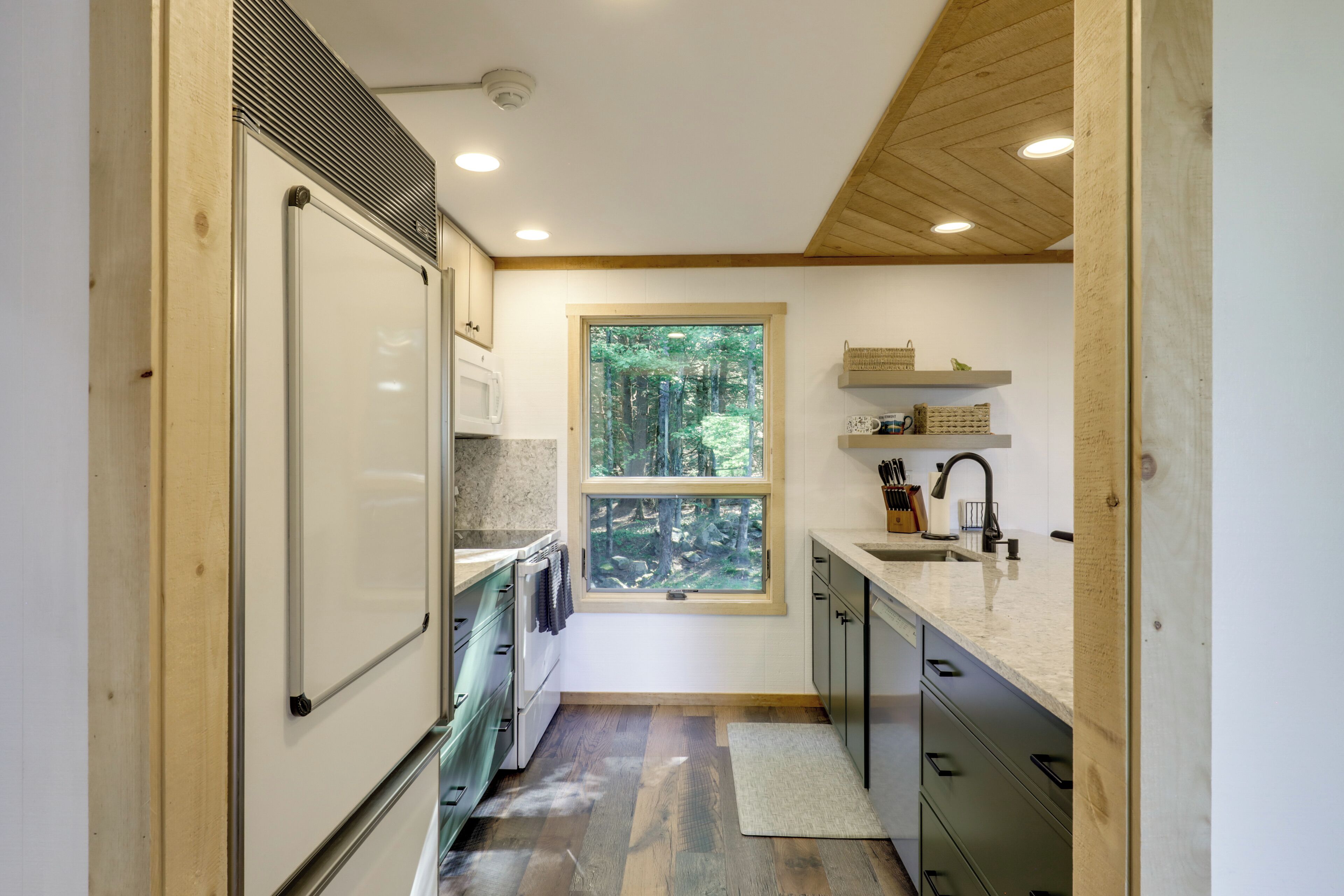 A compact kitchen with a window, wooden ceiling, and built-in appliances.