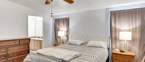 A bedroom with a bed, a nightstand, a dresser, a ceiling fan, and a window with curtains.