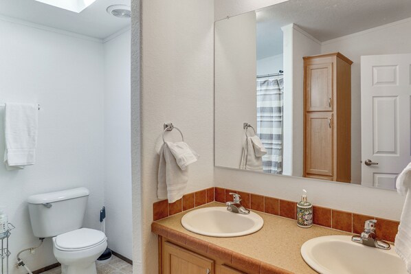 A bathroom with a toilet, two sinks, a mirror, and a cabinet. - Magnolia Manor House: Desert Escape, Mtn Views (Dolan Springs)