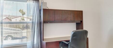 A room with a bunk bed, a desk with a chair, a window with curtains, and a view of a street with cars and buildings.