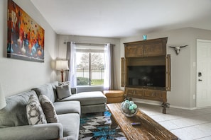 A living room with a sofa, a coffee table with decorative items, a television, and a painting on the wall.