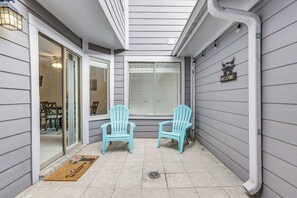 Une terrasse couverte avec deux fauteuils Adirondack bleu clair, un paillasson et une pancarte « Bienvenue » accrochée au mur.