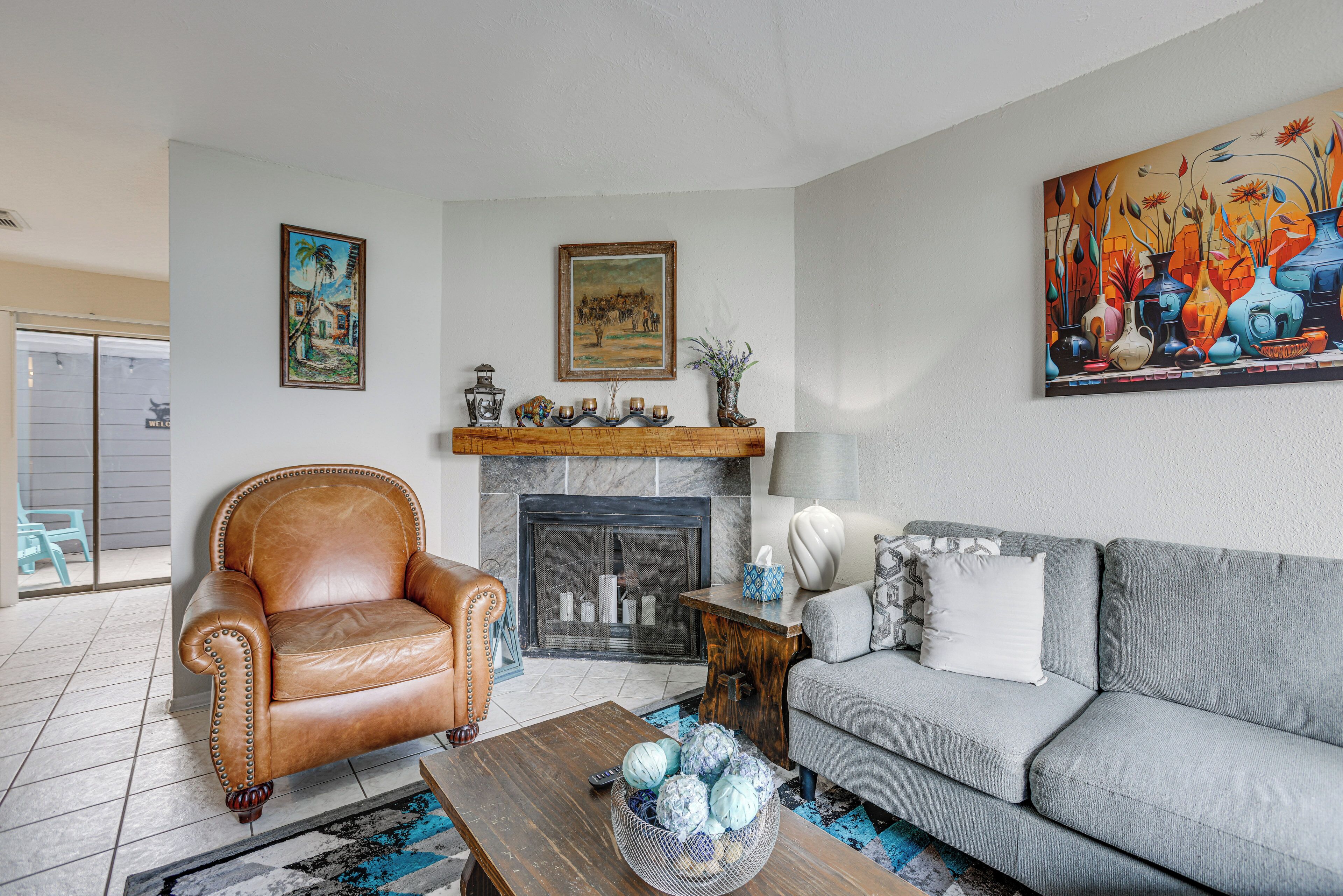 A living room with a fireplace, a sofa, a leather armchair, and a painting on the wall.