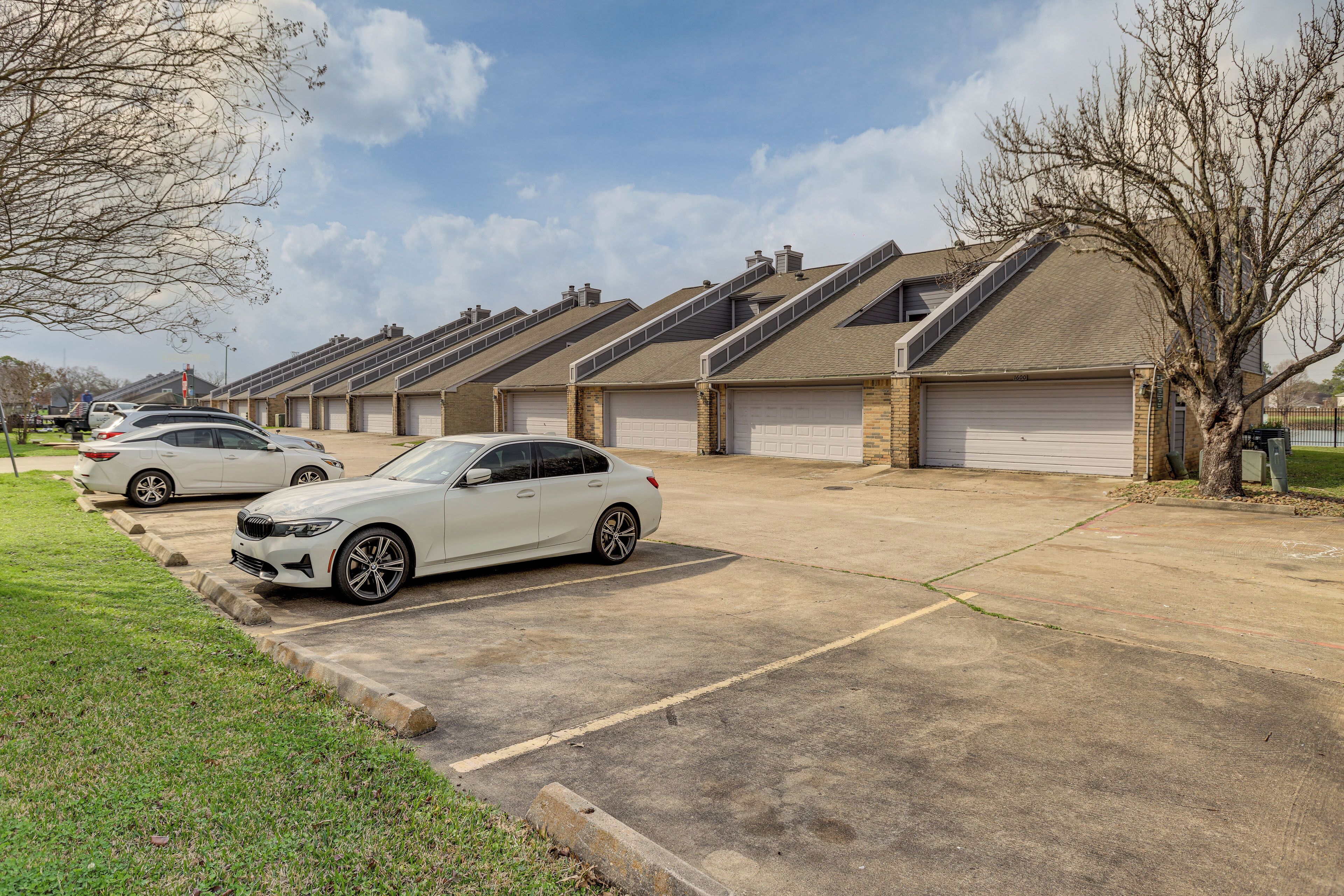 Une rangée de maisons de ville avec des garages attenants, une allée pavée et un espace verdoyant avec des arbres.