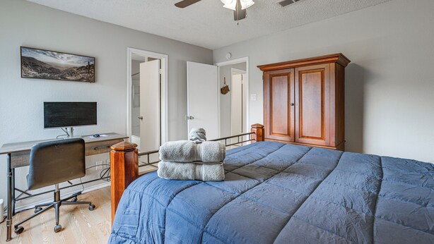 A bedroom with a bed, a desk, a chair, a wardrobe, and a ceiling fan. - Lake-view Townhome w/ Pool Access in Houston Area! (Missouri City)
