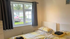 A room with two single beds, a window with curtains, a ceiling light, and a view of a parked car outside. - 2 Bed Cottage - Sleeps 5 - Pets - Parking - Garden (Liskeard)